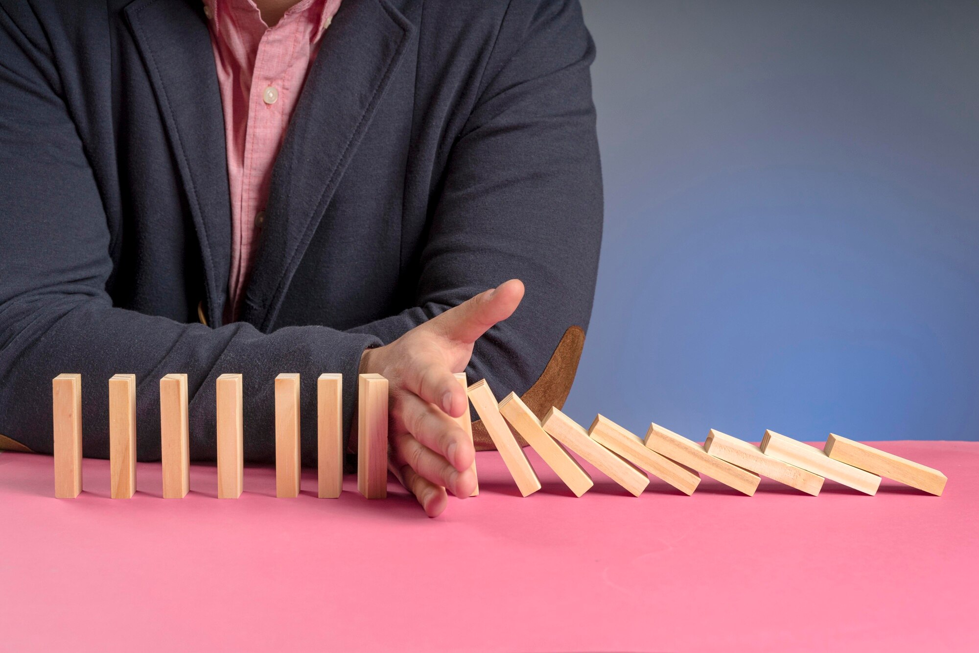 A consultant's hand preventing a chain of dominos from falling, symbolizing proactive risk transformation and effective consulting services.
